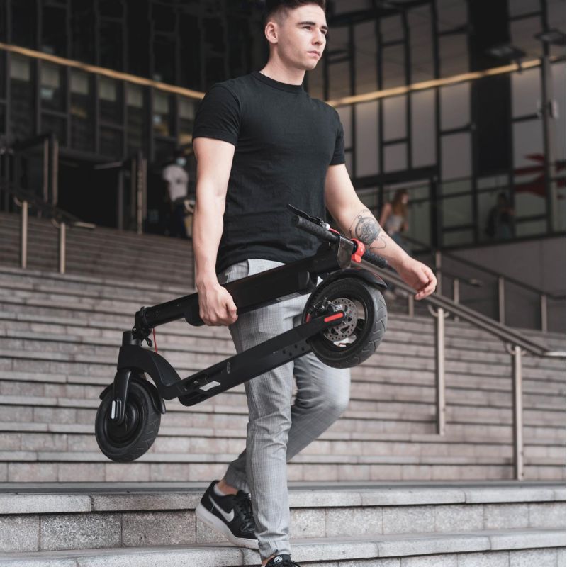 Man carrying a black folded Cruzaa e-scooter on outdoor steps.